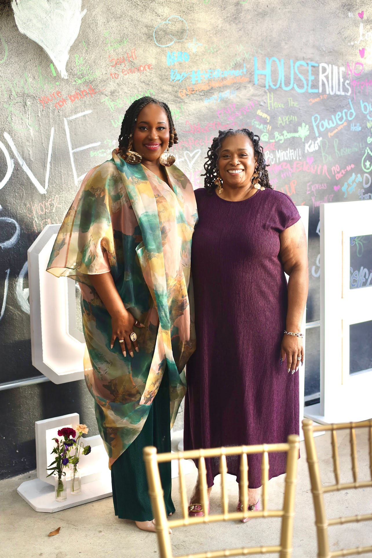 Two guests in front of the House Rules chalkboard wall