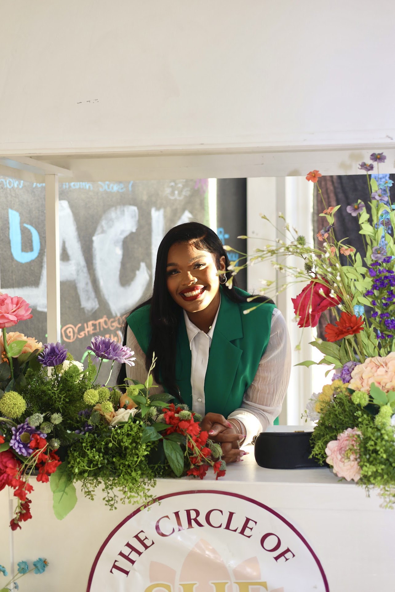 Guest smiling behind the floral-trimmed Circle of SHE booth